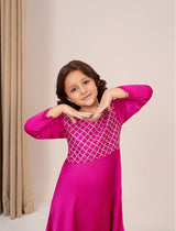 Young girl wearing a pink traditional outfit with a geometric design on a neutral background